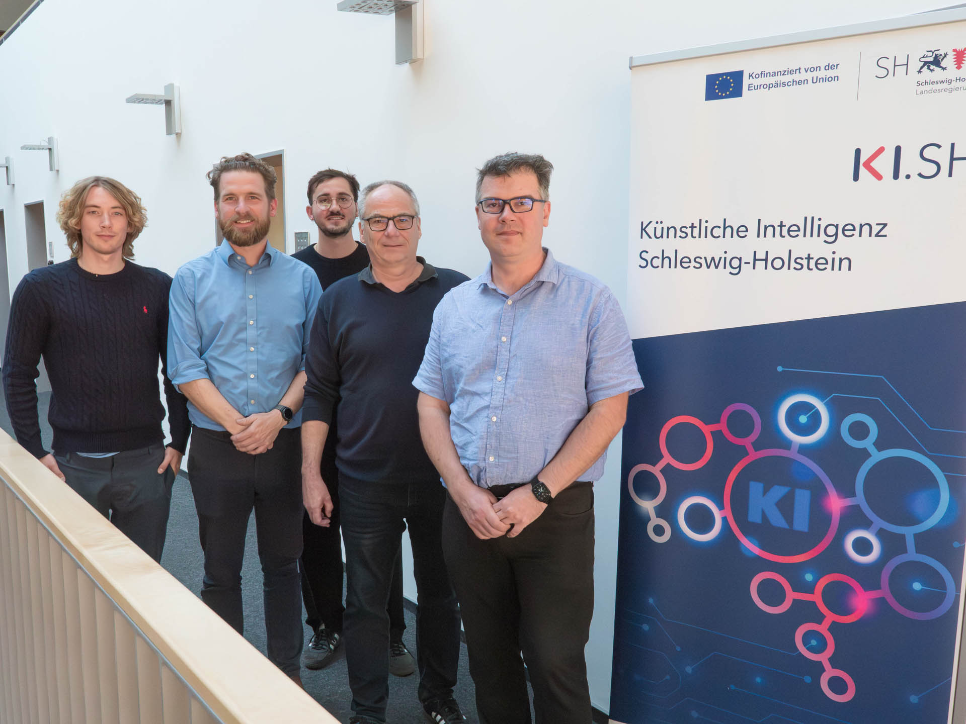 Das Projektteam steht links neben einem KI.SH Roll-Up. V.l.: Lasse Päplow, Prof. Dr. Daniel Böhnke, Josef Küstner (jeweils KI.SH) sowie Christian Müller und Dirk Reinhold (beide Predixxion - WSO GmbH).